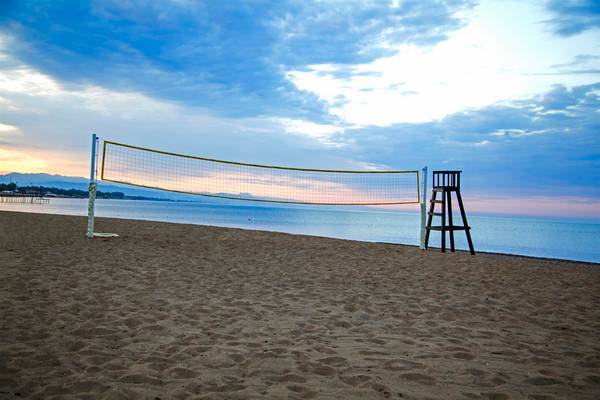 Ein Volleyballnetz steht am Strand bei Sonnenuntergang, dahinter ist das Meer zu sehen.
