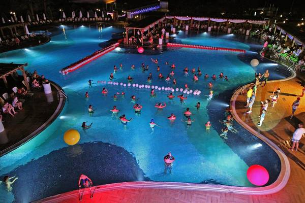 Menschen schwimmen im Pool des Arcanus Side Resort bei Nacht mit Lichteffekten.