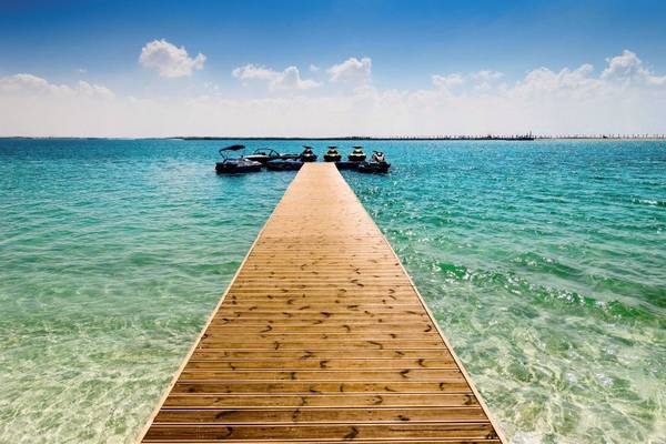 Ein Holzsteg führt vom Ufer ins Wasser, wo mehrere Boote verankert sind.
