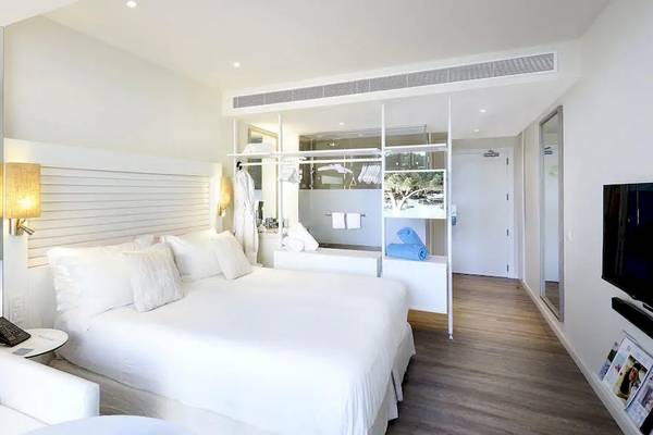 Innenansicht eines Zimmers im ME Ibiza Hotel mit zwei weißen Betten, einem Fernseher und einem Couchtisch.