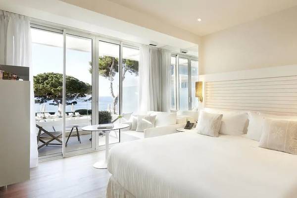 Innenansicht eines Zimmers im ME Ibiza Hotel mit Meerblick, inklusive eines großen Bettes und eines Tisches mit einer Telefon.