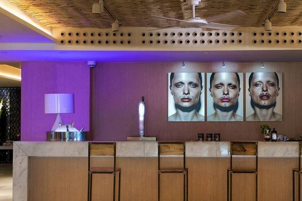 Innenansicht der Bar im ME Ibiza Hotel mit drei Porträts an der Wand, Barhockern und einer Lampe.