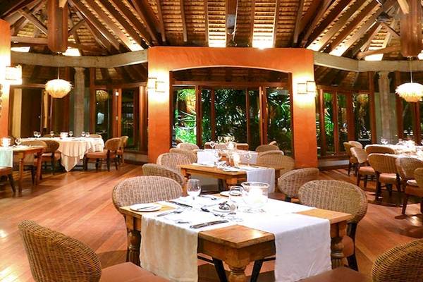 Innenansicht des Speisesaals im Dinarobin Beachcomber Golf Resort & Spa mit Holzböden und großen Fenstern.