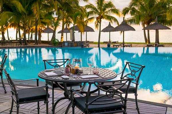 Außenbereich des Dinarobin Beachcomber Golf Resorts mit Swimmingpool und Sonnenuntergang im Hintergrund.