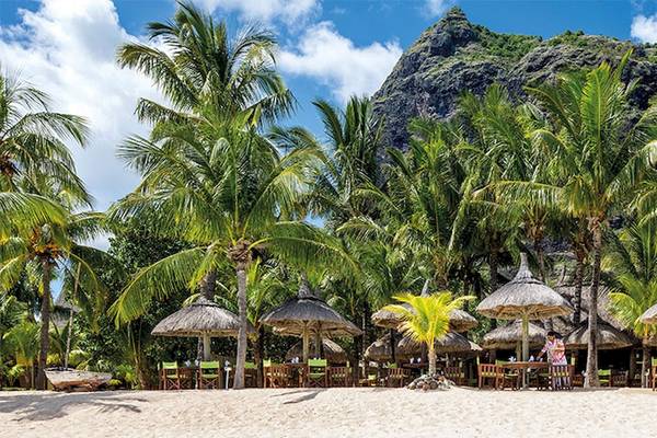 Strand des Dinarobin Beachcomber Golf Resort & Spa mit Palmen und strohgedeckten Hütten.