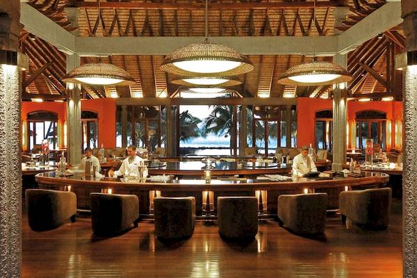 Innenansicht der Bar im Dinarobin Beachcomber Golf Resort & Spa bei Abendstimmung mit Blick auf den Ozean.