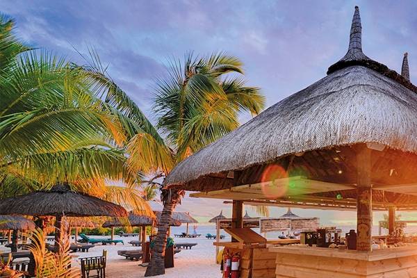 Strandbar im Dinarobin Beachcomber Golf Resort & Spa mit tropischer Kulisse und Sonnenuntergang.