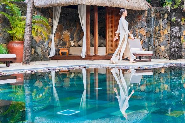 Eine Frau im Bademantel geht neben einem Pool im Dinarobin Beachcomber Golf Resort & Spa.