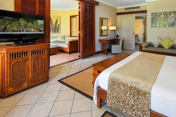Luxuriöses Hotelzimmer im Dinarobin Beachcomber Golf Resort & Spa mit großem Bett, Fernseher und Wohnzimmerbereich.