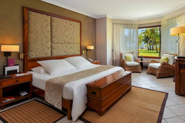 Schlafzimmer im Dinarobin Beachcomber Golf Resort & Spa mit großem Bett, zwei Sesseln, Fernseher und Fenstern zum Garten.