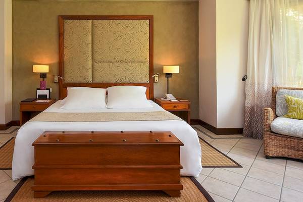 Hotelzimmer mit Doppelbett, Sofa und Korbstuhl neben einem Fenster.