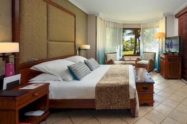 Ein elegant eingerichtetes Zimmer im Dinarobin Beachcomber Golf Resort & Spa mit einem großen Bett, Fernseher und Blick auf den Garten.