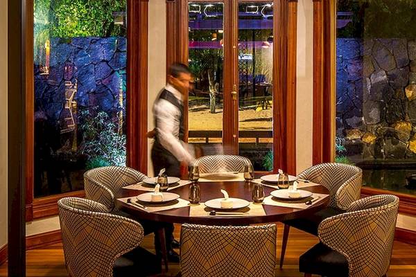 Ein Restaurant-Esstisch mit sechs Stühlen, serviert von einem Kellner im Dinarobin Beachcomber Golf Resort & Spa.