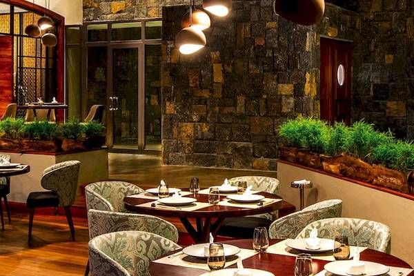 Innenbereich eines eleganten Restaurants im Dinarobin Beachcomber Golf Resort & Spa mit runden Tischen, Stühlen und Holzboden.