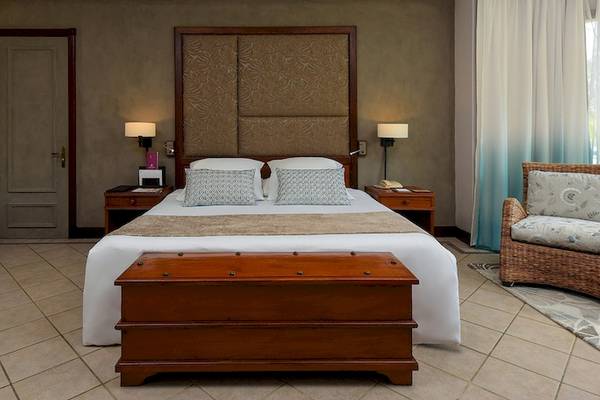 Ein Hotelzimmer mit einem großen Bett, Kissen, Nachttischen und einem Korbstuhl.