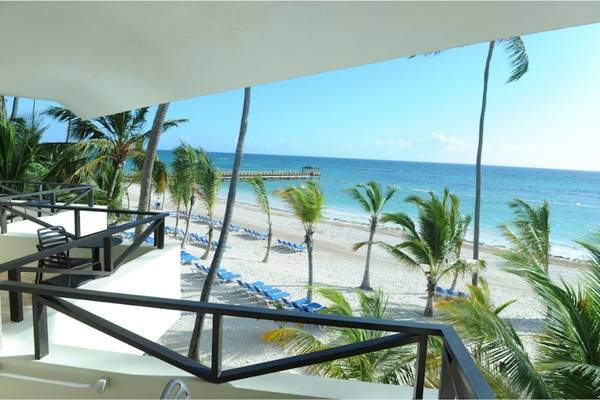 Blick von einer Terrasse auf einen Strand mit Palmen und Liegestühlen am Impressive Premium Punta Cana.