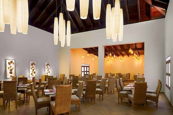 Innenbereich des Impressive Premium Punta Cana Restaurants mit Esstischen, Stühlen und dekorativen Lampen.