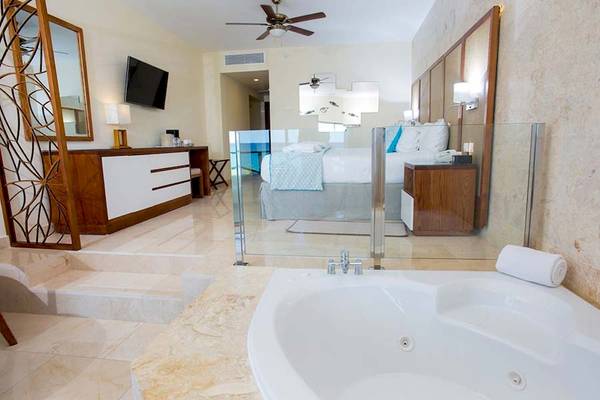 Hotelsuite mit Badewanne und Schlafzimmer, inklusive Fernseher und Glaswänden.