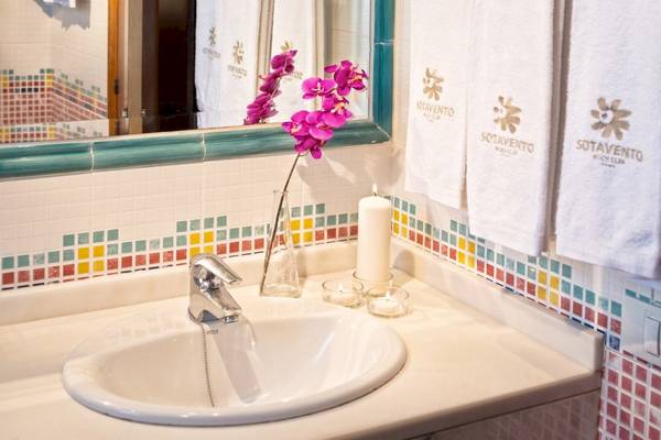 Badezimmer mit Waschbecken, Spiegel und bunten Kacheln im Sotavento Beach Club Hotel.