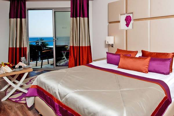 Ein elegantes Hotelzimmer mit einem großen Bett, Blick auf das Meer und einem kleinen Tisch mit Früchten.