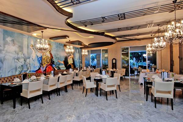 Innenbereich des Restaurants im Botanik Platinum Hotel mit einer großen Wandmalerei, weißen Stühlen und Tischen, und Kronleuchtern.