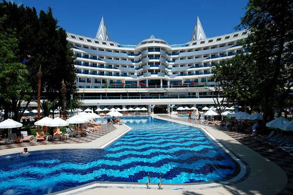 Außenansicht des Botanik Platinum Hotels mit großem Schwimmbad und Sonnenliegen.