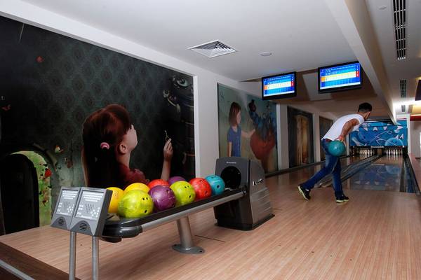 Ein Mann spielt Bowling im Botanik Platinum Hotel mit bunten Kugeln und Monitoren an der Wand.