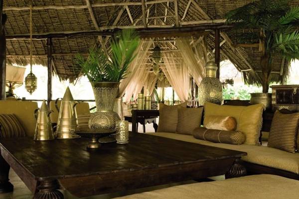 Innenbereich des Breezes Beach Club & Spa Zanzibar mit braunem Tisch, Kissen und Pflanzen.