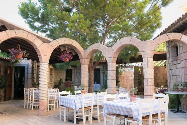Terrasse des Golden Bay Beach Hotels mit blau-weiß karierten Tischdecken und Stühlen unter Bögen