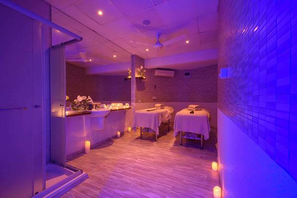 Spa-Behandlungsraum im Golden Bay Beach Hotel mit zwei Behandlungstischen, Kerzen und violetten Wänden.
