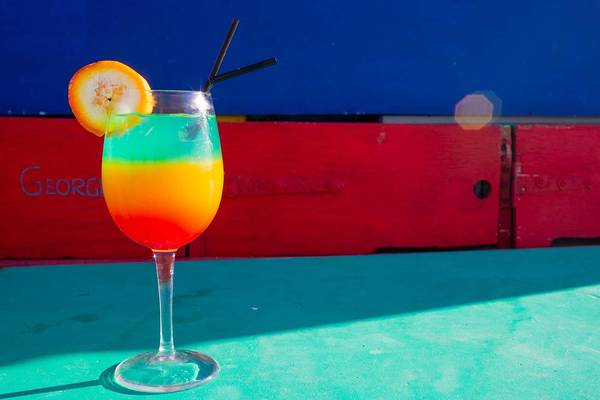 Ein bunter Cocktail in einem Glas auf einem Tisch vor einer roten gemauerten Wand.