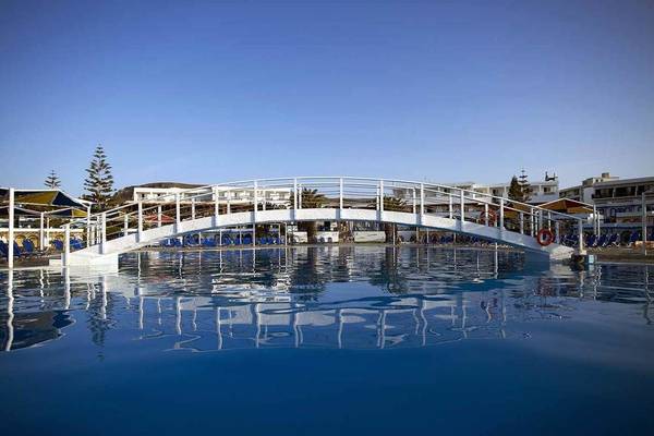 Außenpool des Mitsis Rinela Beach Hotels mit einer Brücke und Sonnenliegen.