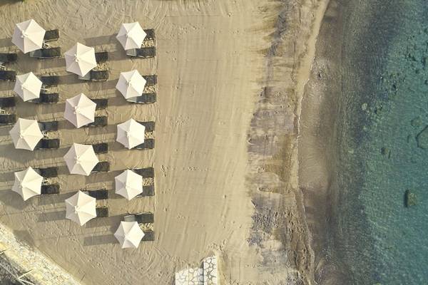 Luftaufnahme von Liegestühlen und Sonnenschirmen am Strand des Minos Palace Hotel & Suites.