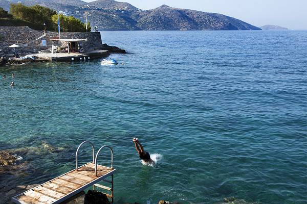 Person springt ins Meer am Minos Palace Hotel & Suites, umgeben von Klippen und Bergen.