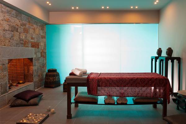 Spa-Bereich im Minos Palace Hotel & Suites mit Massagetisch, Kissen, Kamin und Glaswand.