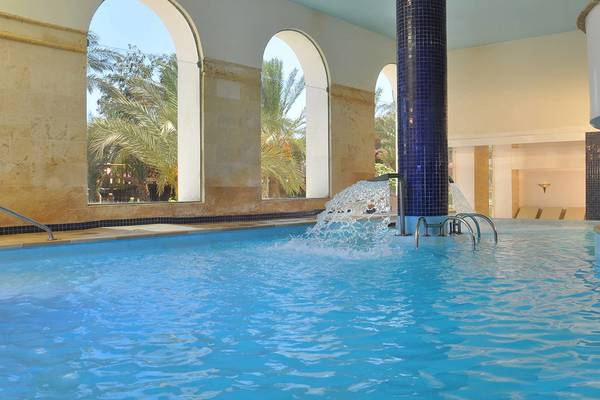 Ein großer Innenpool im Sheraton Sharm Hotel mit Wasserfontäne und bogenförmigen Fenstern.