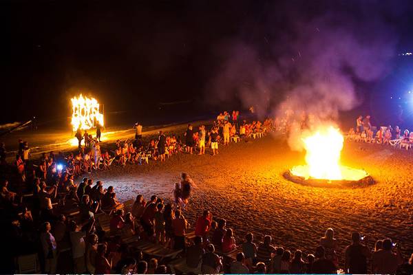 Menschen versammeln sich auf dem Strand für ein Feuer am Abend vor dem Side Sun Hotel.