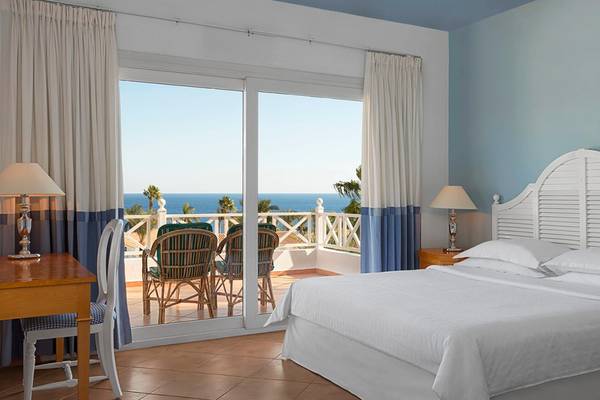 Schlafzimmer im Sheraton Sharm Hotel mit Meerblick, großen Schiebetüren und einer Terrasse mit Möbeln.