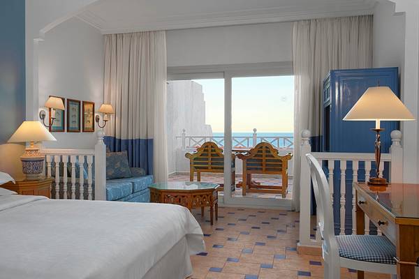 Zimmer im Sheraton Sharm Hotel mit Meerblick, Doppelbett, Schreibtisch und Balkon.