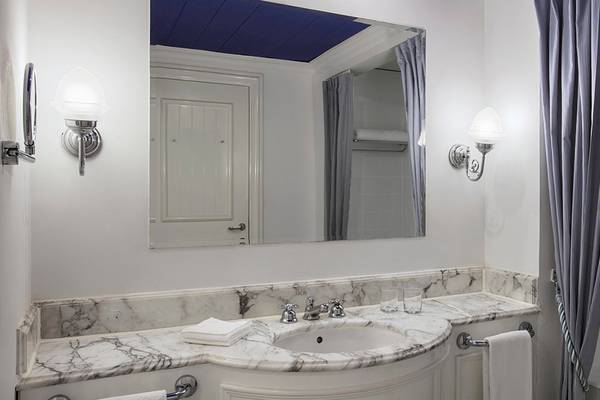 Ein Badezimmer mit weißem Marmor, Spiegel, Waschbecken, Badewanne, und Lampen.