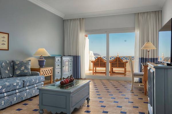 Wohnzimmer des Sheraton Sharm Hotel mit Blick auf das Meer, inklusive Sofa, Tisch, Lampen und Fernseher.