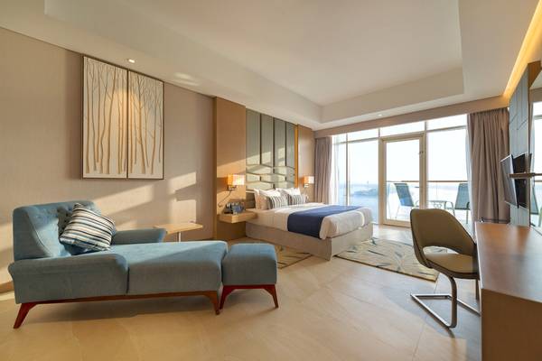 Innenansicht einer Suite im Royal Central Hotel The Palm mit Bett, Möbeln und Meerblick.