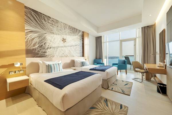 Doppelzimmer im Royal Central Hotel The Palm mit zwei Betten, Blick auf das Meer und modernen Möbeln.