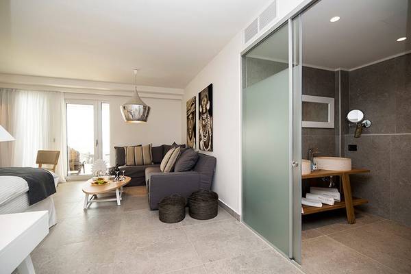 Innenansicht eines Zimmers im Insula Alba Resort & Spa mit Bett, Sofa, Tisch und Badezimmer.