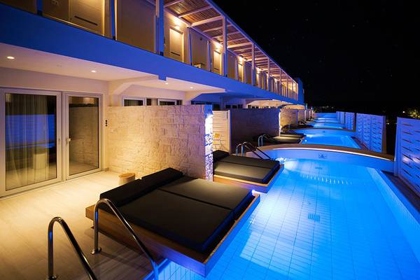Außenpool des Insula Alba Resorts & Spa bei Nacht mit blauen Lichtern und Liegen.