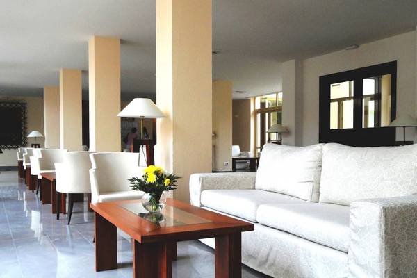 Hotellobby mit Sofa, Tisch mit Blumen, weißen Sesseln und Säulen im Hintergrund.
