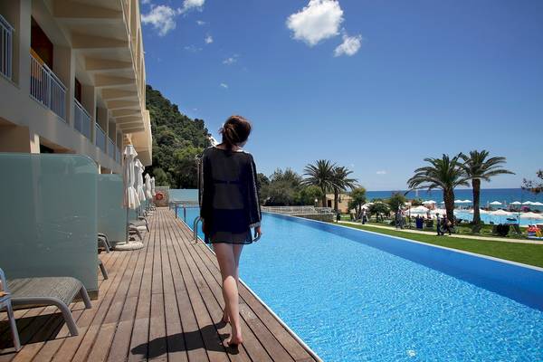 Frau geht am Pool des Domes of Corfu Hotel entlang, während sie in Richtung des Ozeans schaut