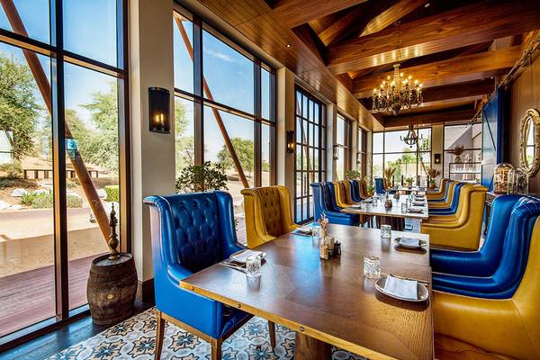 Innenraum des Restaurants im Ritz-Carlton Ras Al Khaimah, Al Wadi Desert, mit blauen und gelben Stühlen und Tischen.