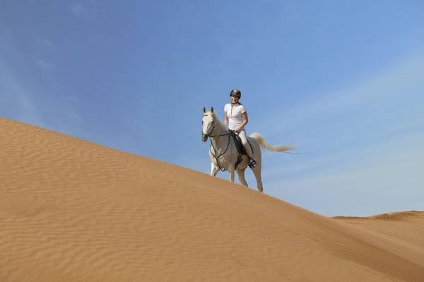 Eine Frau reitet ein weißes Pferd in der Wüste des Ritz-Carlton Ras Al Khaimah, Al Wadi Desert.