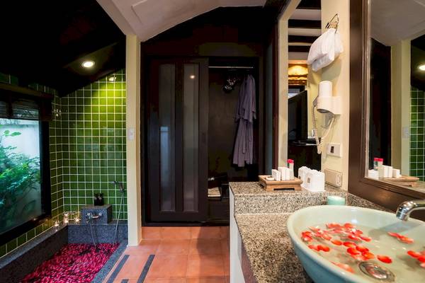 Badezimmer im Hotel Khao Lak Emerald Beach Resort & Spa mit grünen Kacheln, rotem Boden und Badewanne mit Rosenblättern.